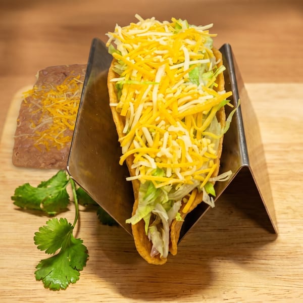 Hard shell taco with shredded cheese and lettuce, served with refried beans and cilantro.
