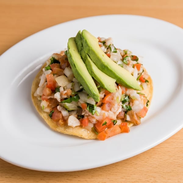 A tostada topped with ceviche, diced tomatoes, onions, cilantro, and avocado slices.