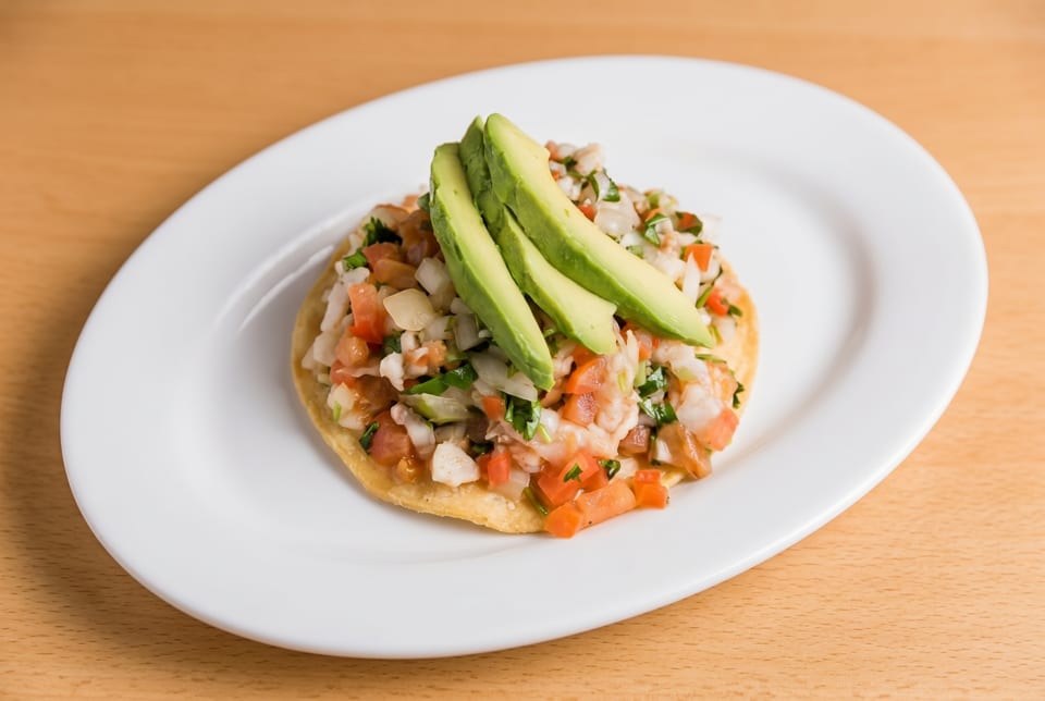 A tostada topped with ceviche, diced tomatoes, onions, cilantro, and avocado slices.