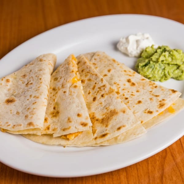 Cheese quesadillas with guacamole and sour cream on a white plate.