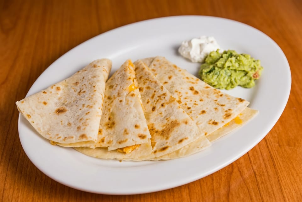 Cheese quesadillas with guacamole and sour cream on a white plate.