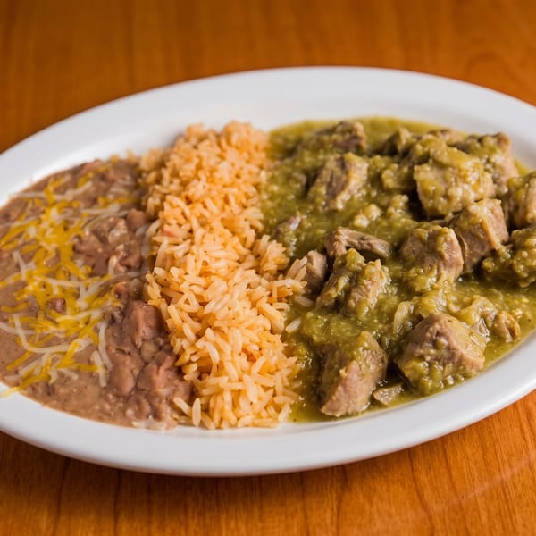 A white oval plate with chile verde, Spanish rice, and refried beans topped with cheese.