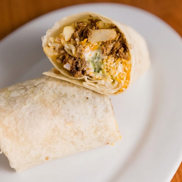 Two burritos on a white plate, one cut in half revealing meat, cheese, and sauce.