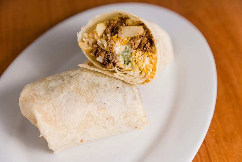 Two burritos on a white plate, one cut in half revealing meat, cheese, and sauce.