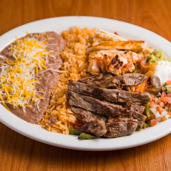 A white plate with steak, chicken, rice, refried beans with cheese, guacamole, and pico de gallo.