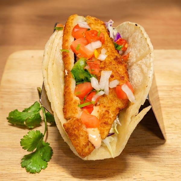 Crispy fish taco with diced tomatoes, onions, and cilantro, served on a wooden board.