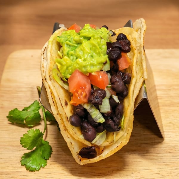 A vibrant taco filled with guacamole, black beans, diced tomatoes, and lettuce on a wooden board.