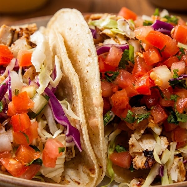 Two grilled chicken tacos with shredded cabbage, red onion, and diced tomatoes on a plate.