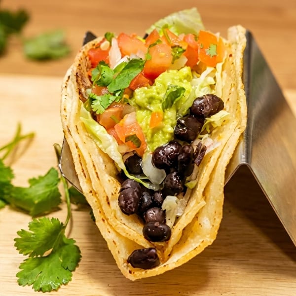 A fresh taco filled with black beans, guacamole, lettuce, and pico de gallo in a metal holder.