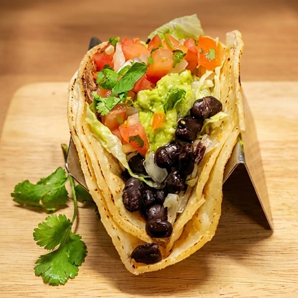 A vibrant taco filled with black beans, guacamole, lettuce, and pico de gallo on a wooden board.