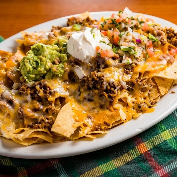 A large plate of loaded nachos with melted cheese, ground beef, guacamole, sour cream, and pico de gallo.