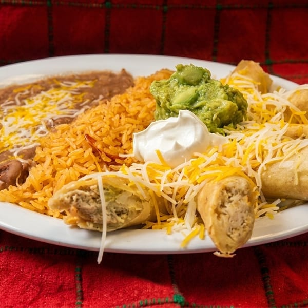 A plate of taquitos, rice, refried beans, guacamole, sour cream, and shredded cheese.